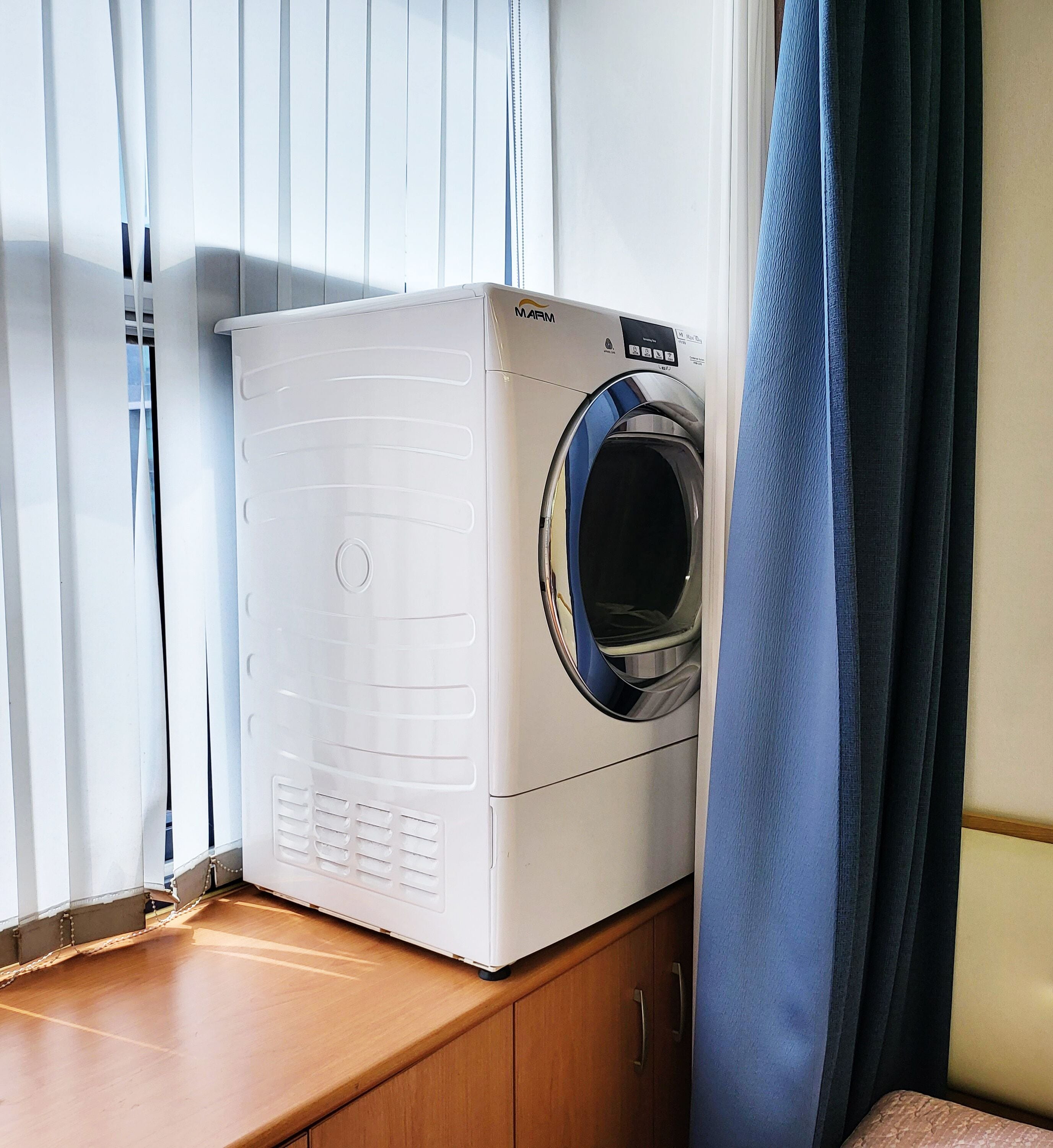A front-loading white washer and dryer unit with a control panel, placed on a wooden cabinet.