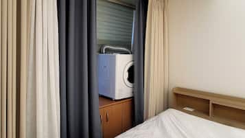 A hotel room with a bed, a wooden headboard, a wardrobe, and a white appliance, possibly a washing machine, in the background.