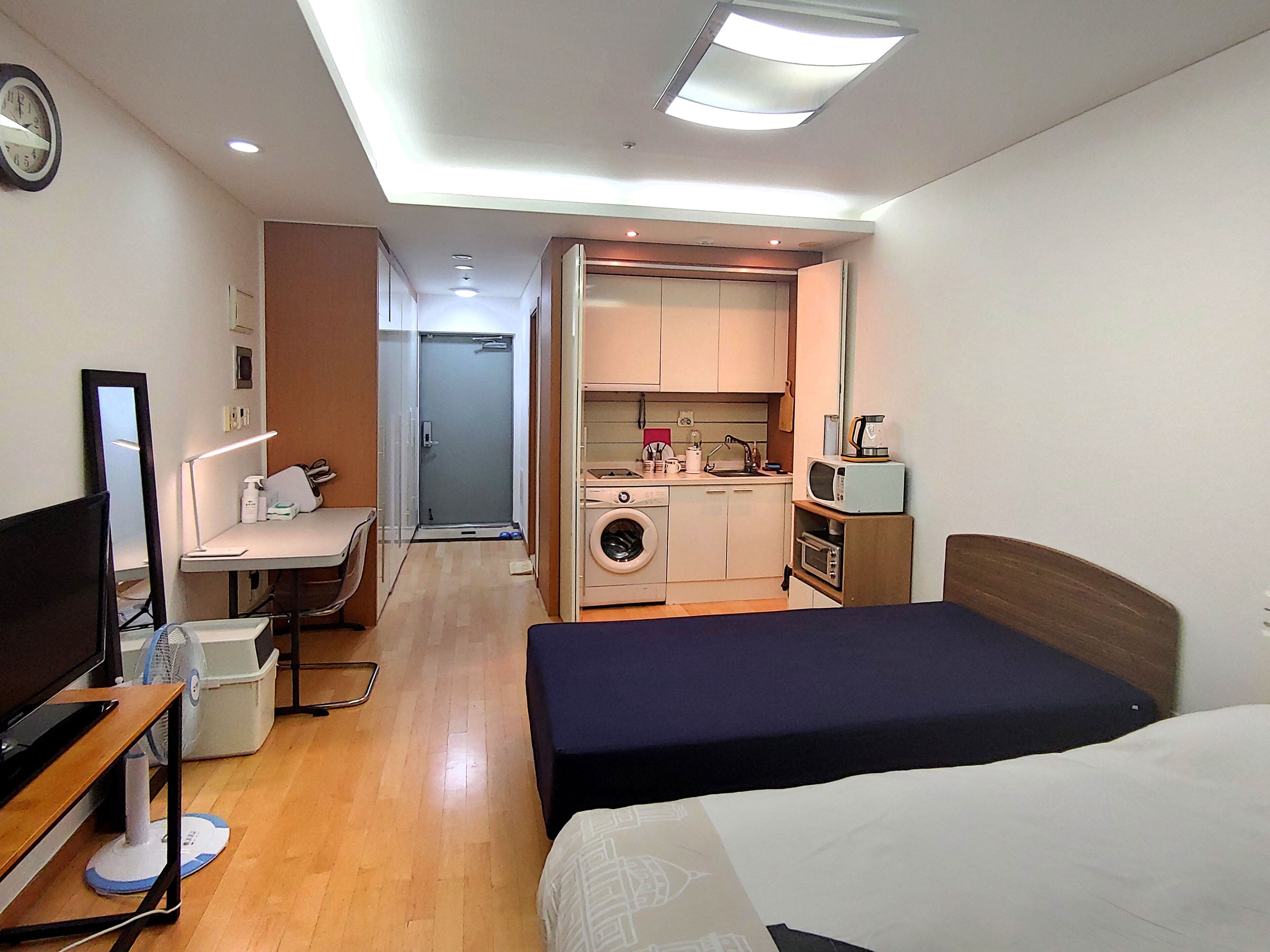 Een compacte hotelkamer met een bed, een bureau met een computer, een wasmachine en een kitchenette.