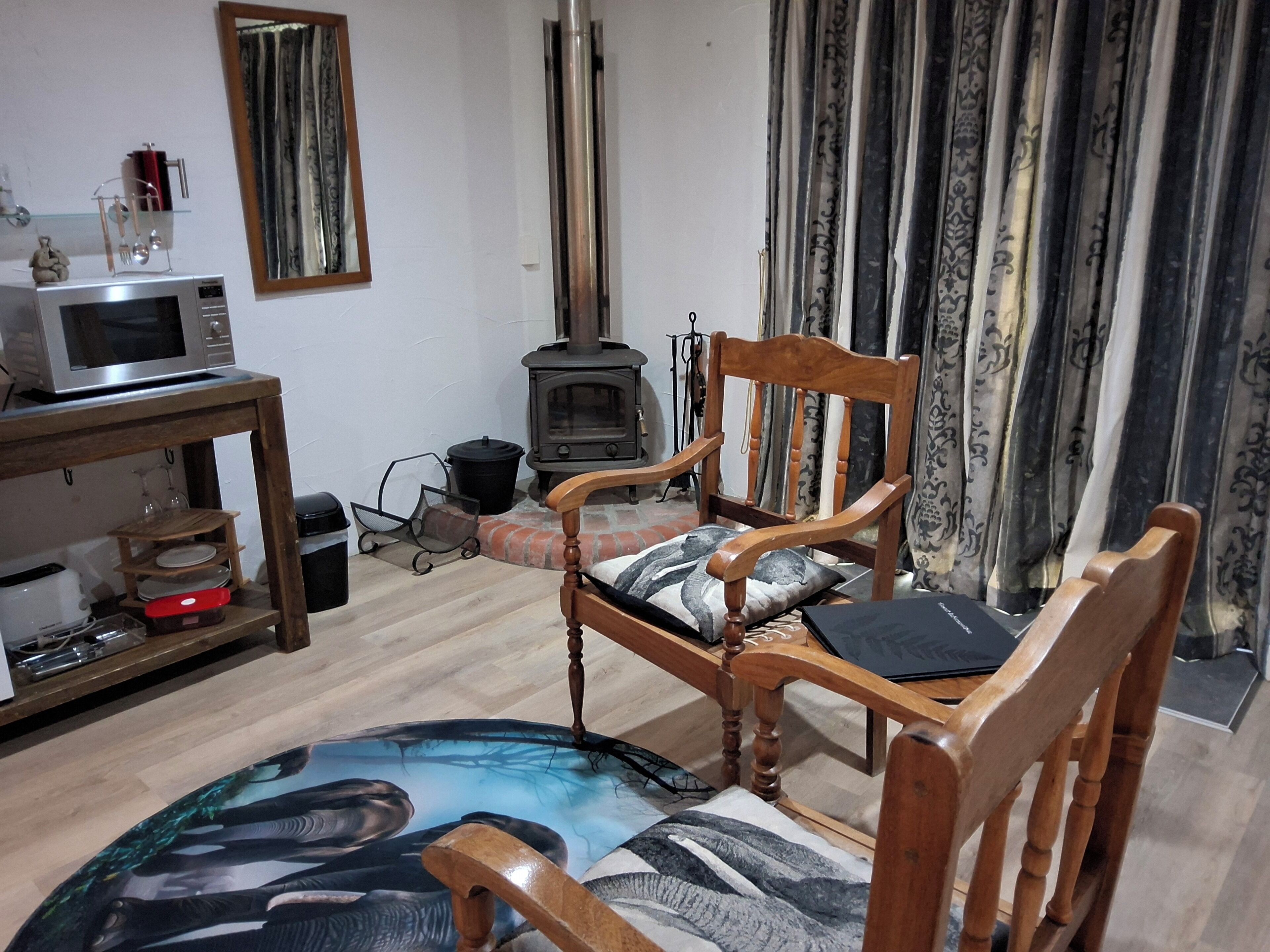 A living room with a wooden chair, a table with a microwave, a fireplace, and curtains.
