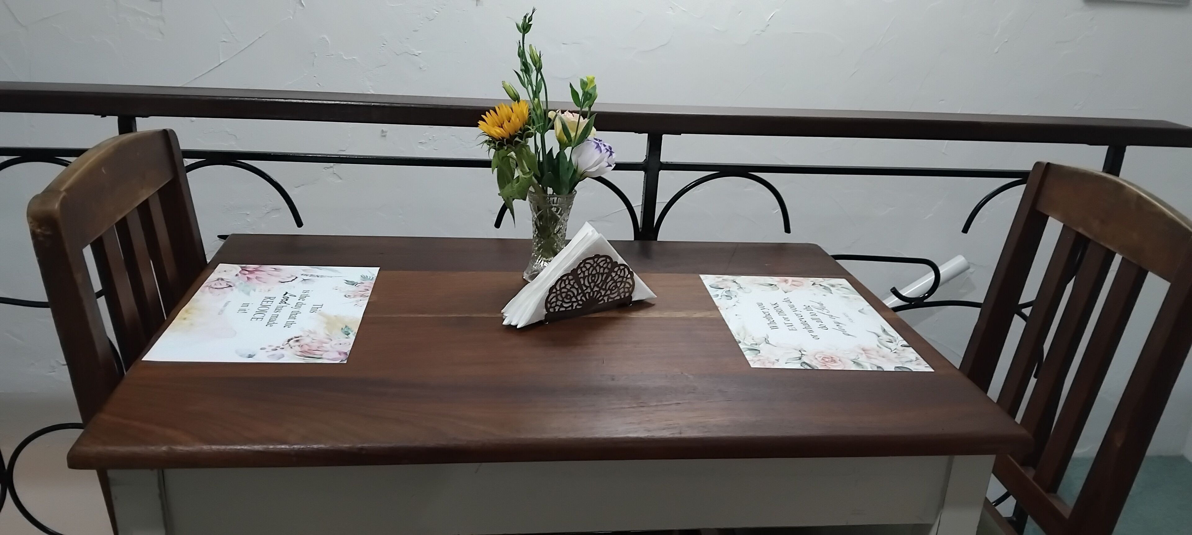 A wooden table with two chairs, a vase with flowers, and a menu on the table.