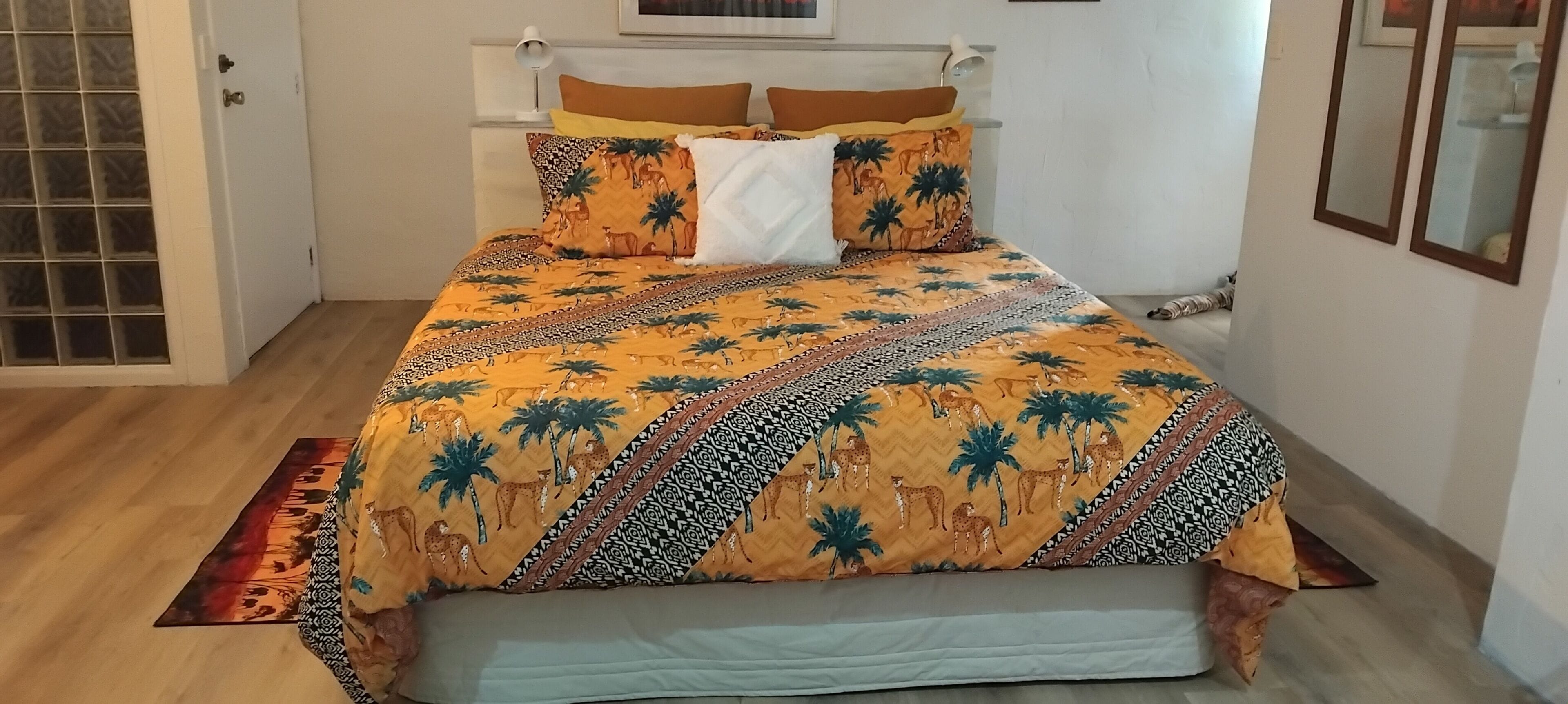 A bed with a patterned bedspread, a bedside lamp, and a window with blinds.