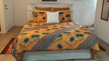 A bed with a patterned bedspread, a bedside lamp, and a window with blinds.