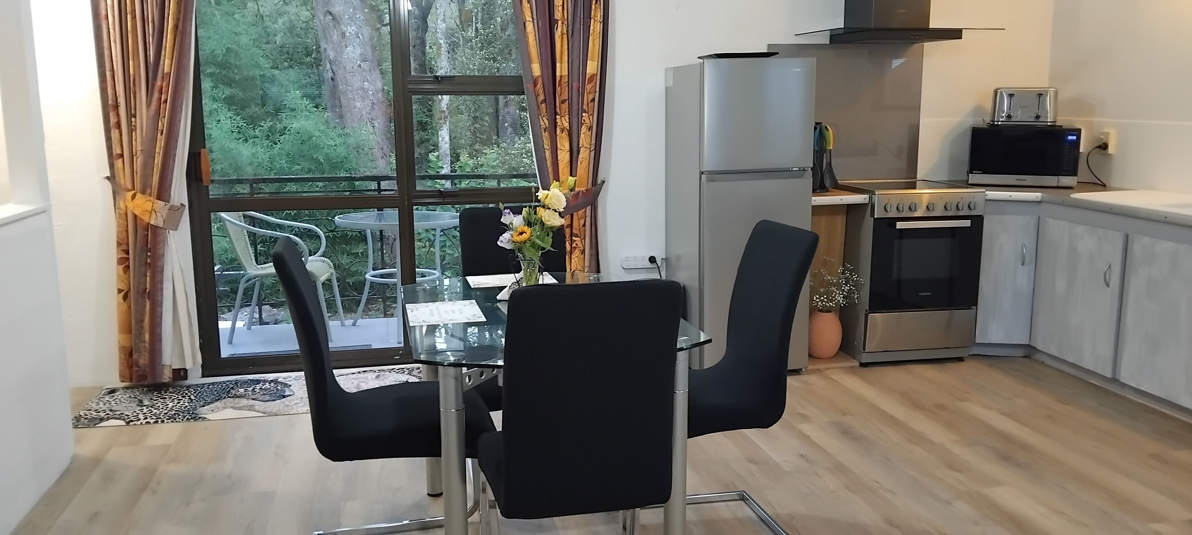 Une cuisine moderne équipée d’un réfrigérateur, d’une cuisinière et d’un four à micro-ondes. On y trouve une table à manger avec des chaises et un vase rempli de fleurs.