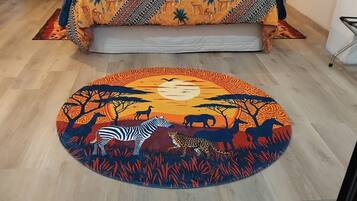 Una alfombra redonda con una escena de sabana, una cama con ropa de cama estampada y una silla.