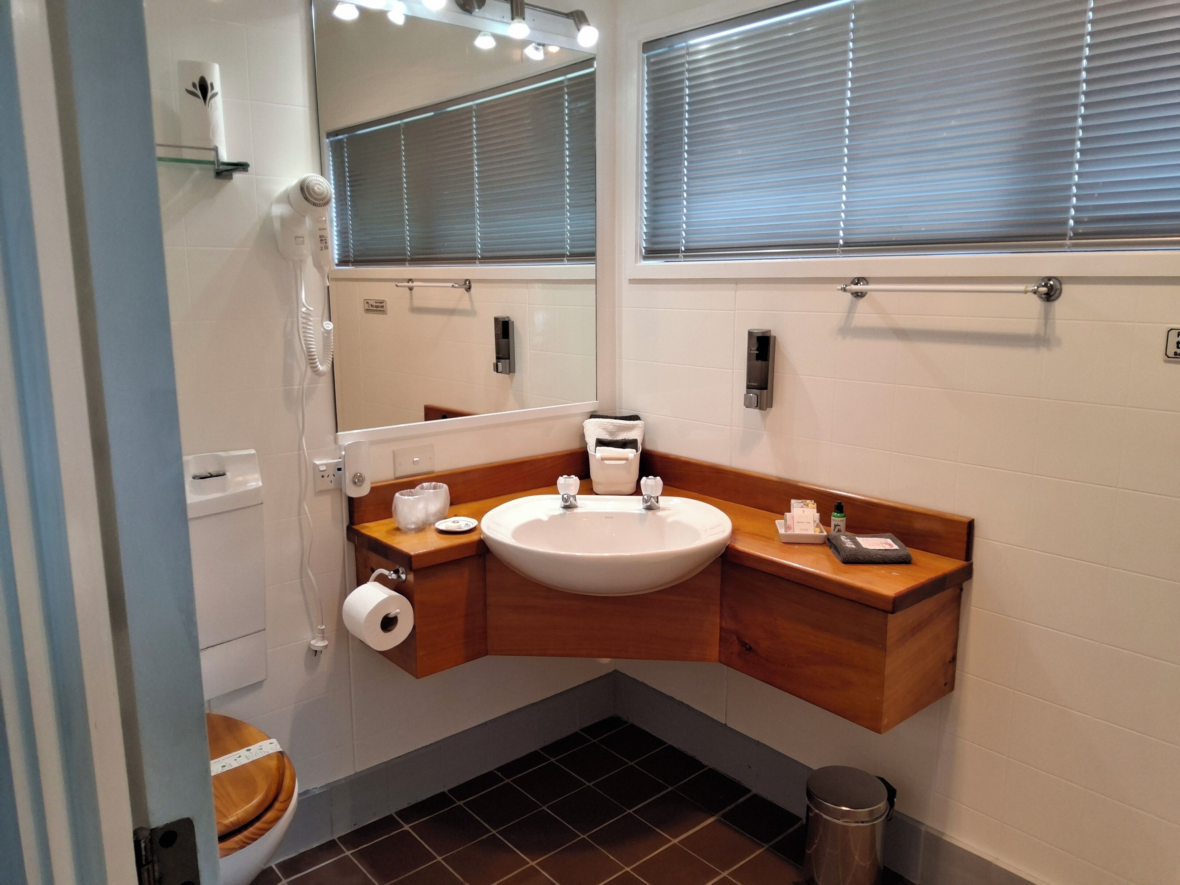 A bathroom with a wooden vanity, a sink, a mirror, a toilet, and a trash can.
