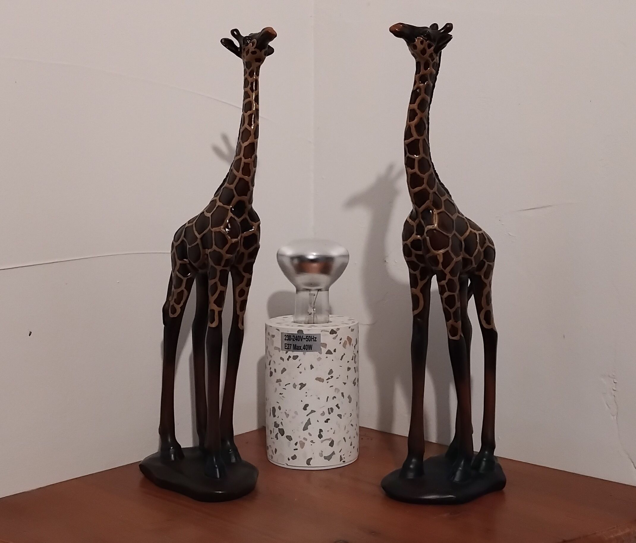 Two giraffe figurines on a wooden surface with a speckled pedestal in between.