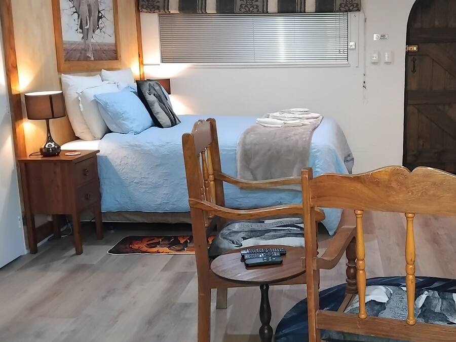 A bedroom with a bed, bedside table, lamp, chair, and a small table with a remote control.