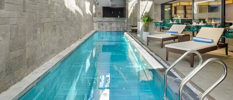Una piscina interior con agua cristalina, rodeada de sillas de descanso y una zona de bar.