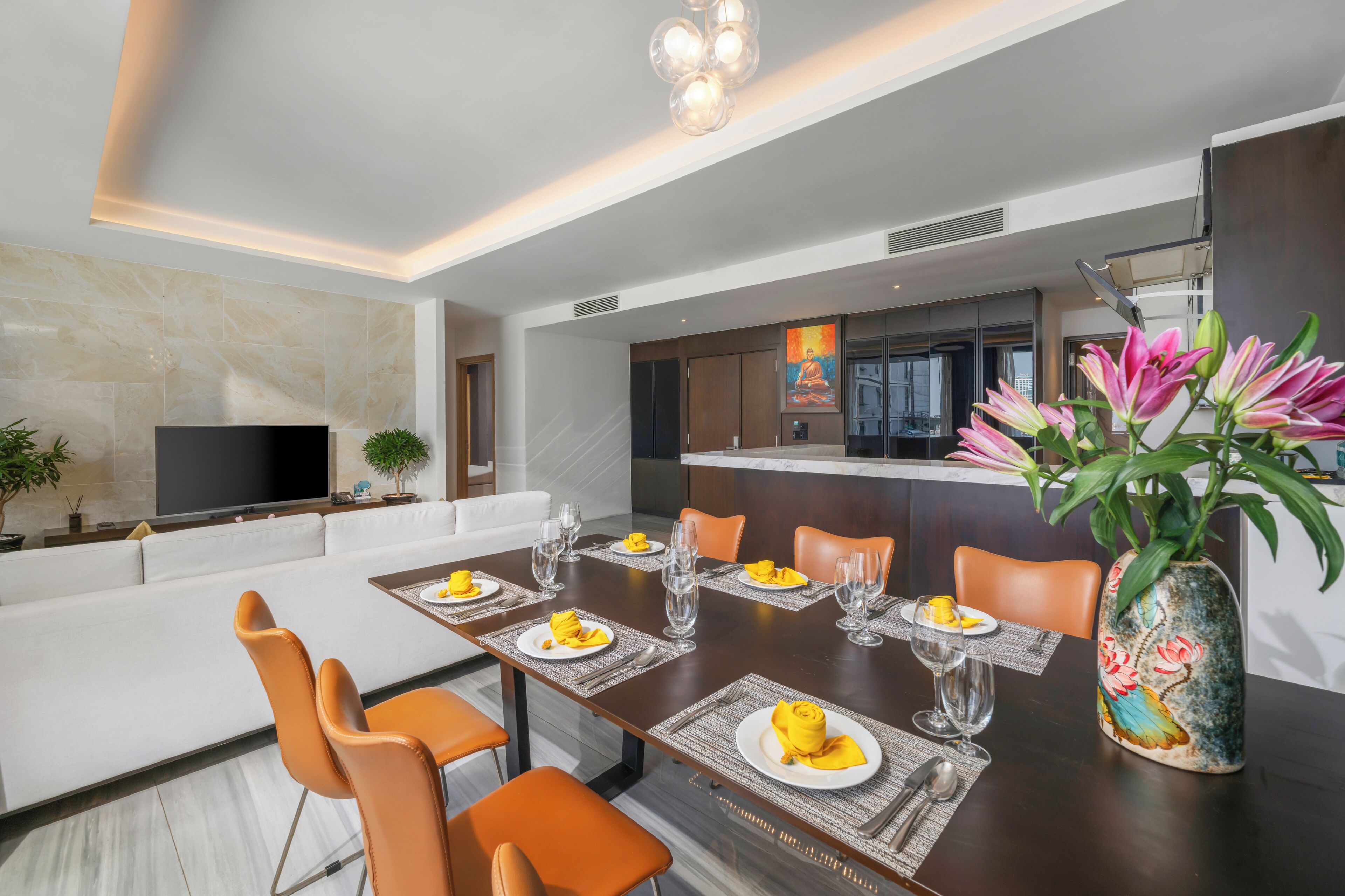 A modern dining area with a long table set for four, surrounded by orange chairs.