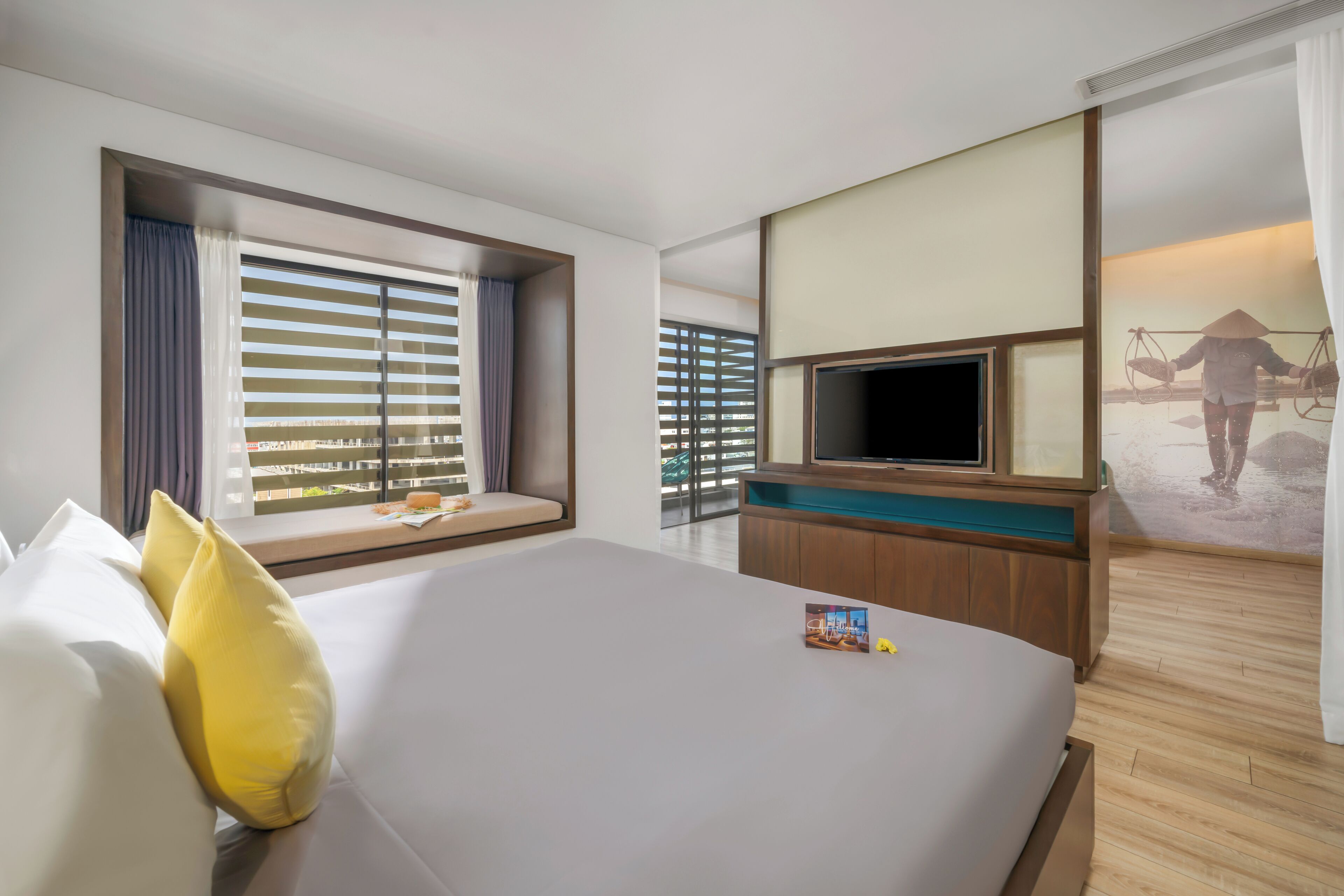 A hotel room with a large bed, a TV, a window with blinds, and a view of a balcony.