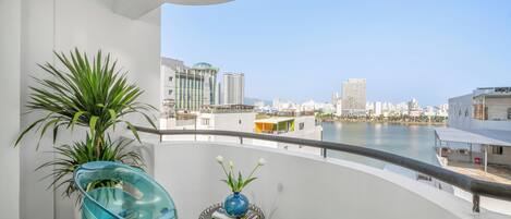 A balcony with a view of a city skyline, a potted plant, and a blue chair.