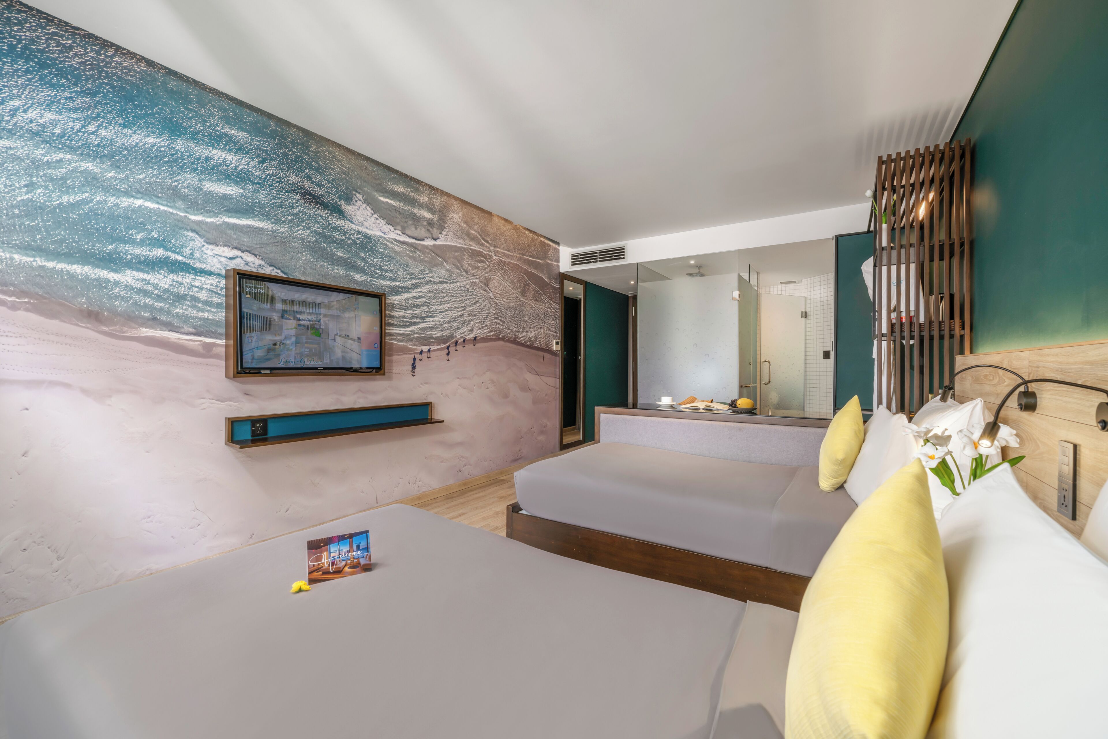 A modern hotel room with two beds, a large wall mural, a mounted TV, and a bathroom visible through an open door.