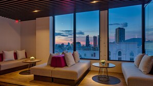 A modern lounge area with a city view, featuring a sofa set, a round table, and a wooden floor. - Satya Da Nang Hotel Han Market (Da Nang)