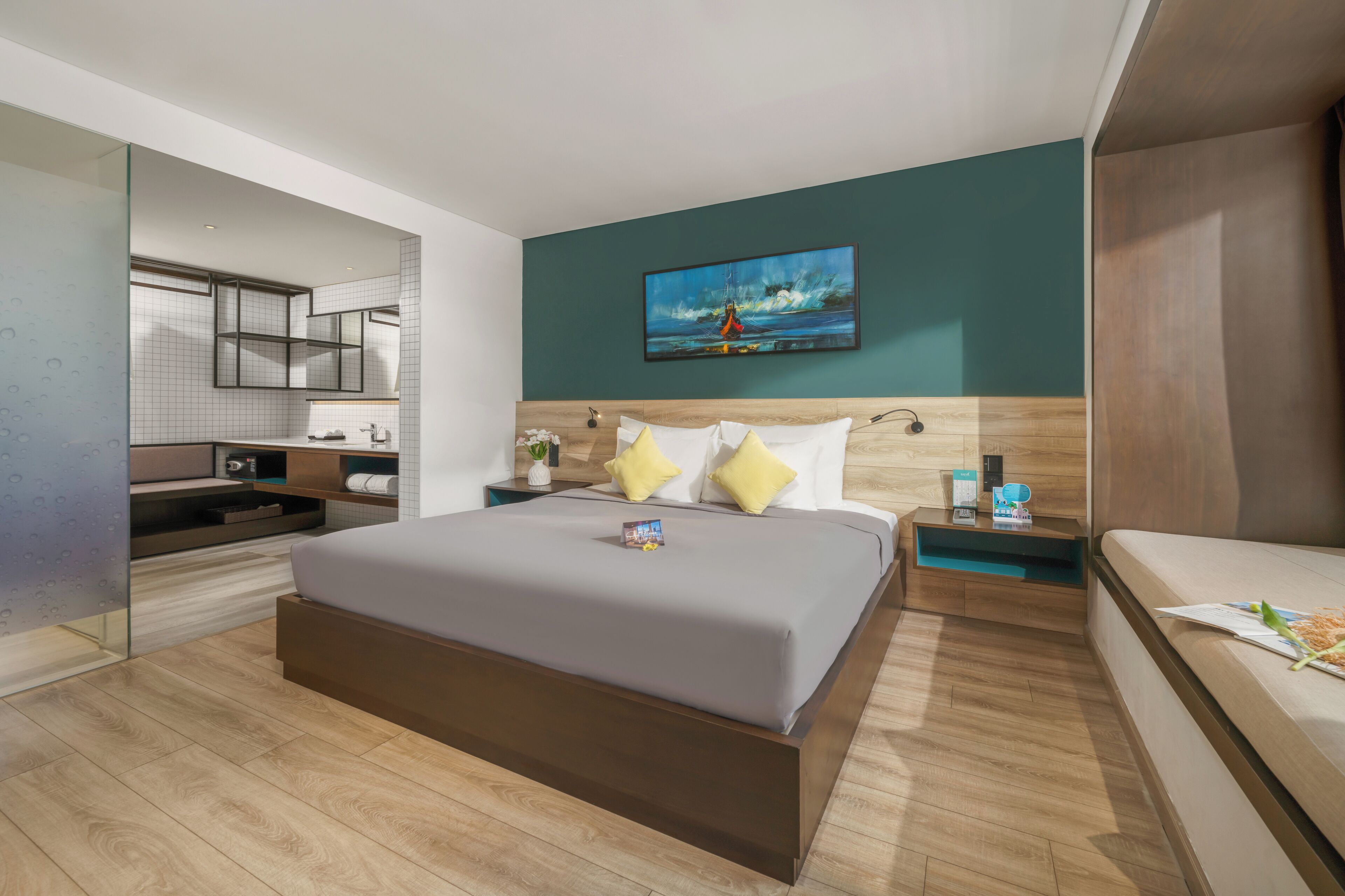 Habitación de hotel moderna con una cama grande, una mesita de noche con una lámpara, una mesita auxiliar pequeña con un teléfono y un cuadro en la pared.