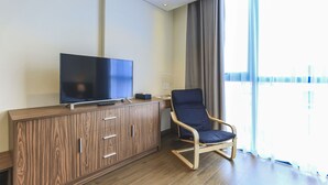 Moderni huone, jossa on litteänäyttöinen televisio puisen kaapin päällä, sininen tuoli ja suuri ikkuna, jossa on verhot.