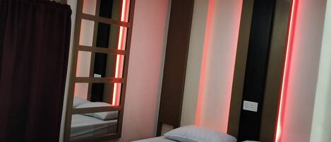 A single bed with a white mattress and pillows, a red curtain, and a ceiling with recessed lighting.