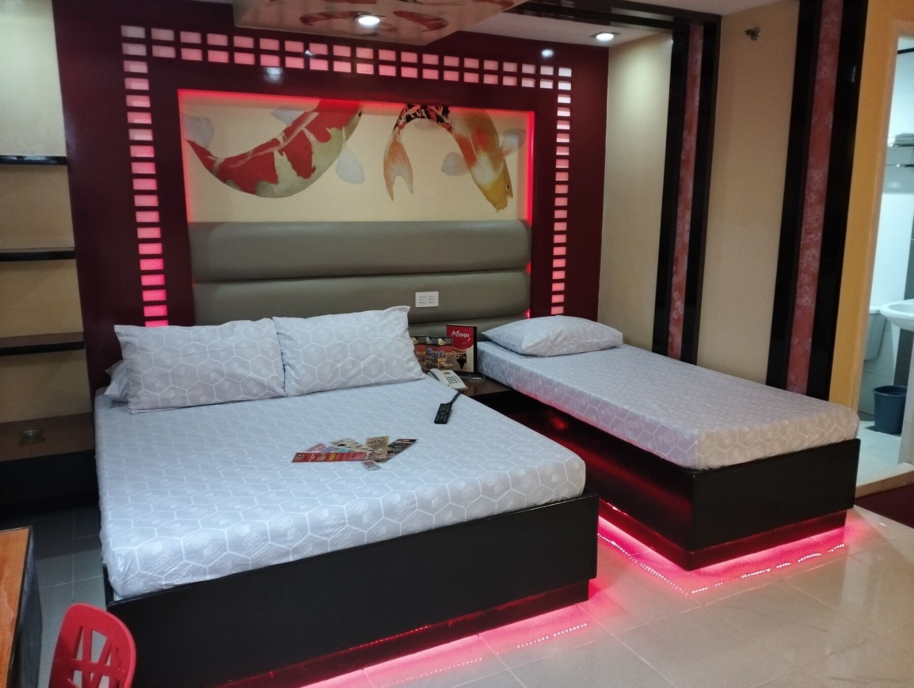 Een moderne hotelkamer met een groot bed, een klein bed en een rode stoel.