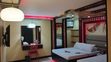A hotel room with a bed, a desk with a chair, a mirror, and a ceiling light.