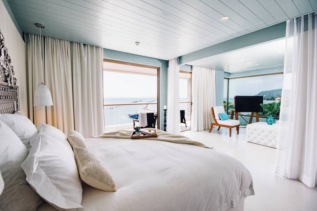 A spacious bedroom with a large bed, a view of the sea, and a balcony with a chair and table.