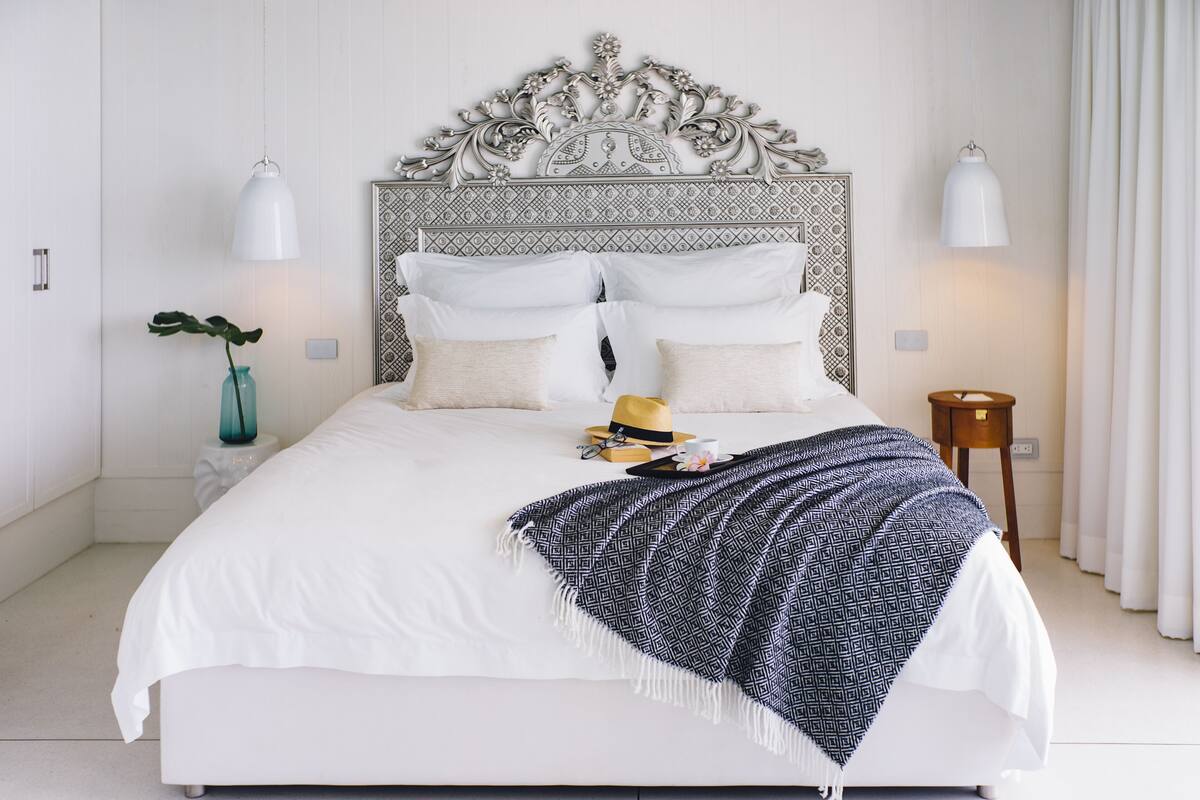 A neatly made bed with a patterned throw blanket, a small bedside table with a lamp, and a decorative headboard.