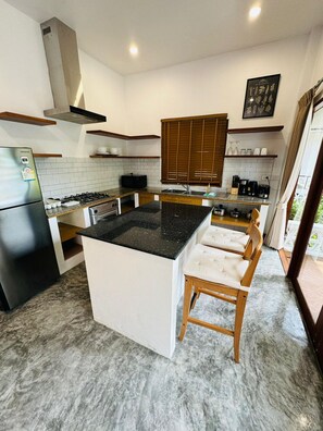 A modern kitchen with a central island, wooden cabinets, and a stainless steel refrigerator.
