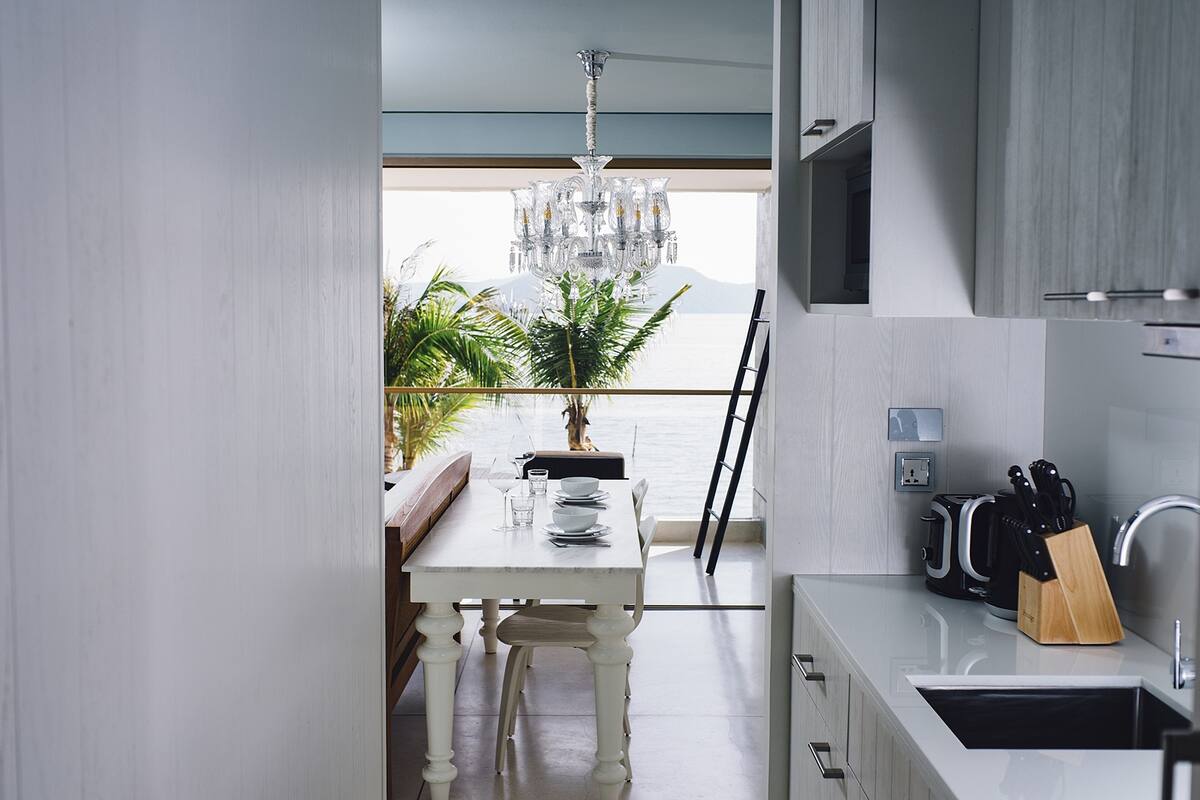 A modern kitchen with a view of the sea, a dining area with a white table, and a chandelier.