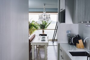 A modern kitchen with a view of the sea, a dining area with a white table, and a chandelier.
