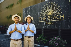 Two people standing in front of a sign that reads "THE BEACH SAMU".