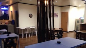 A dining area with tables and chairs, a wooden partition, and a wall-mounted clock. - Lolo Bob's Bed And Breakfast (El Nido)