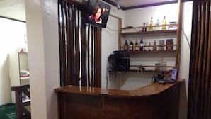 A reception area with a wooden reception desk, a television mounted on the wall, and shelves with various bottles. - Lolo Bob's Bed And Breakfast (El Nido)