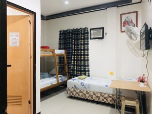A room with a bunk bed, a desk, a chair, a small stool, a fan, and a picture on the wall. - Lolo Bob's Bed And Breakfast (El Nido)
