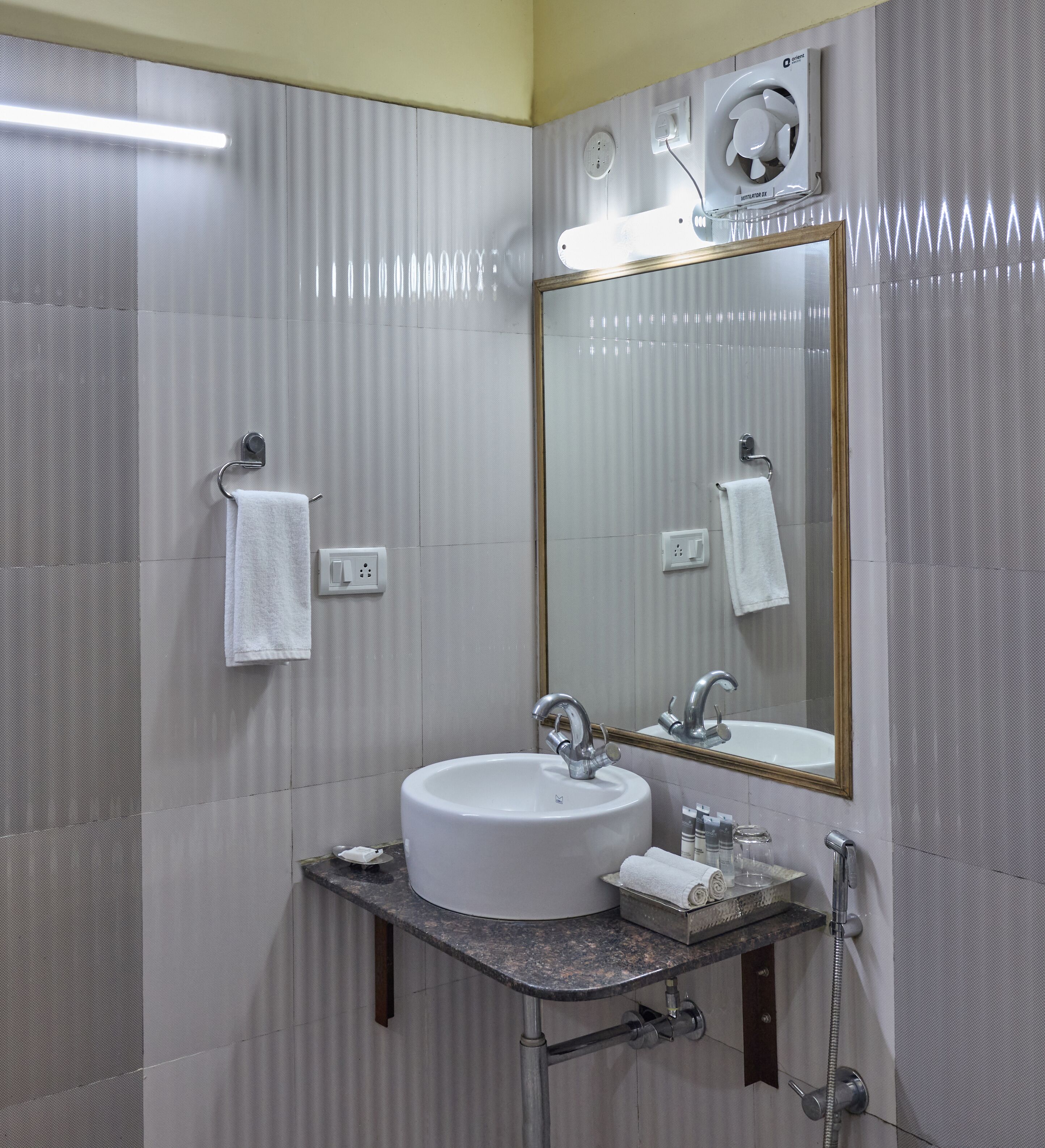 Un baño con lavamanos, espejo, toallero y unidad de ventilación.