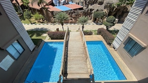 A view of a swimming pool with a wooden deck leading to it, surrounded by buildings and a rocky landscape. - Golden Amoon Resort (Hoskote)