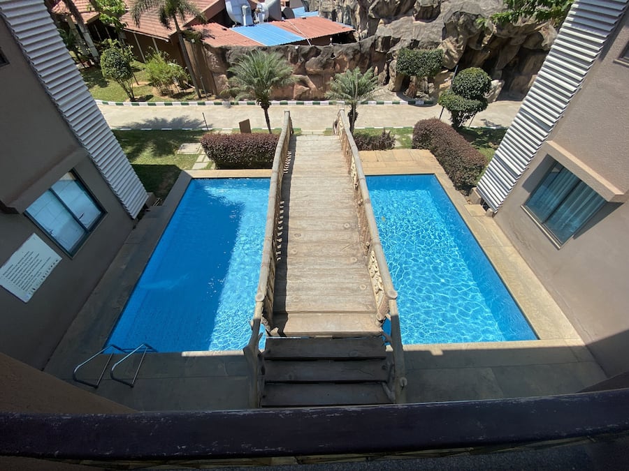 Vista de una piscina con un muelle de madera que la conecta, rodeada de edificios y un paisaje rocoso.