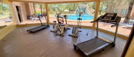 A gym with treadmills, an elliptical, and a stationary bike, with large windows overlooking a pool and outdoor area.