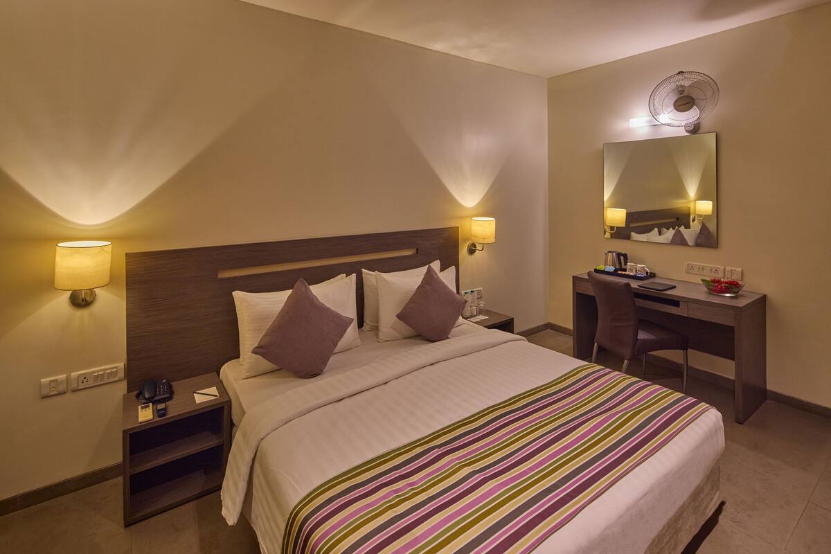 A hotel room with a bed, bedside lamps, a desk, and a mirror.