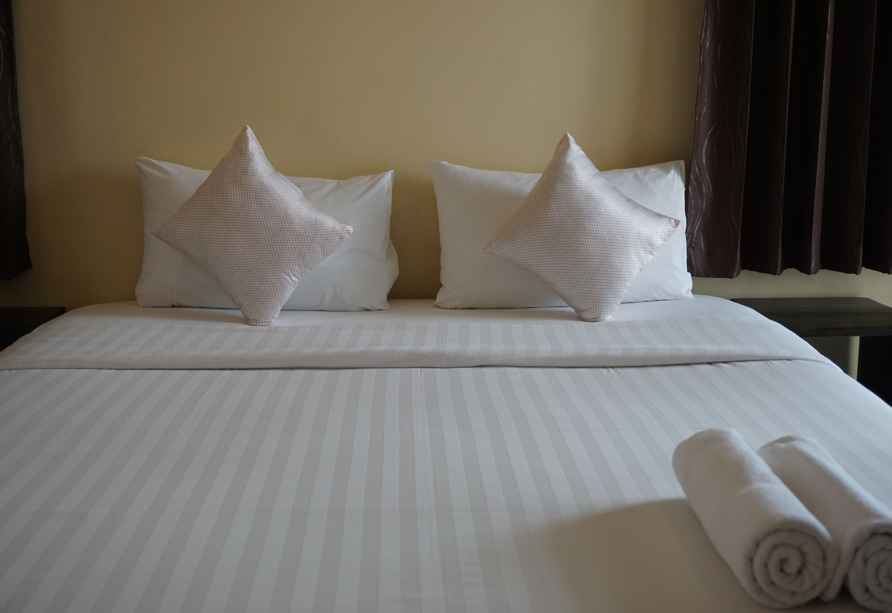 Una cama bien hecha con ropa de cama a rayas, dos almohadas con forma de estrella y toallas enrolladas a un lado.