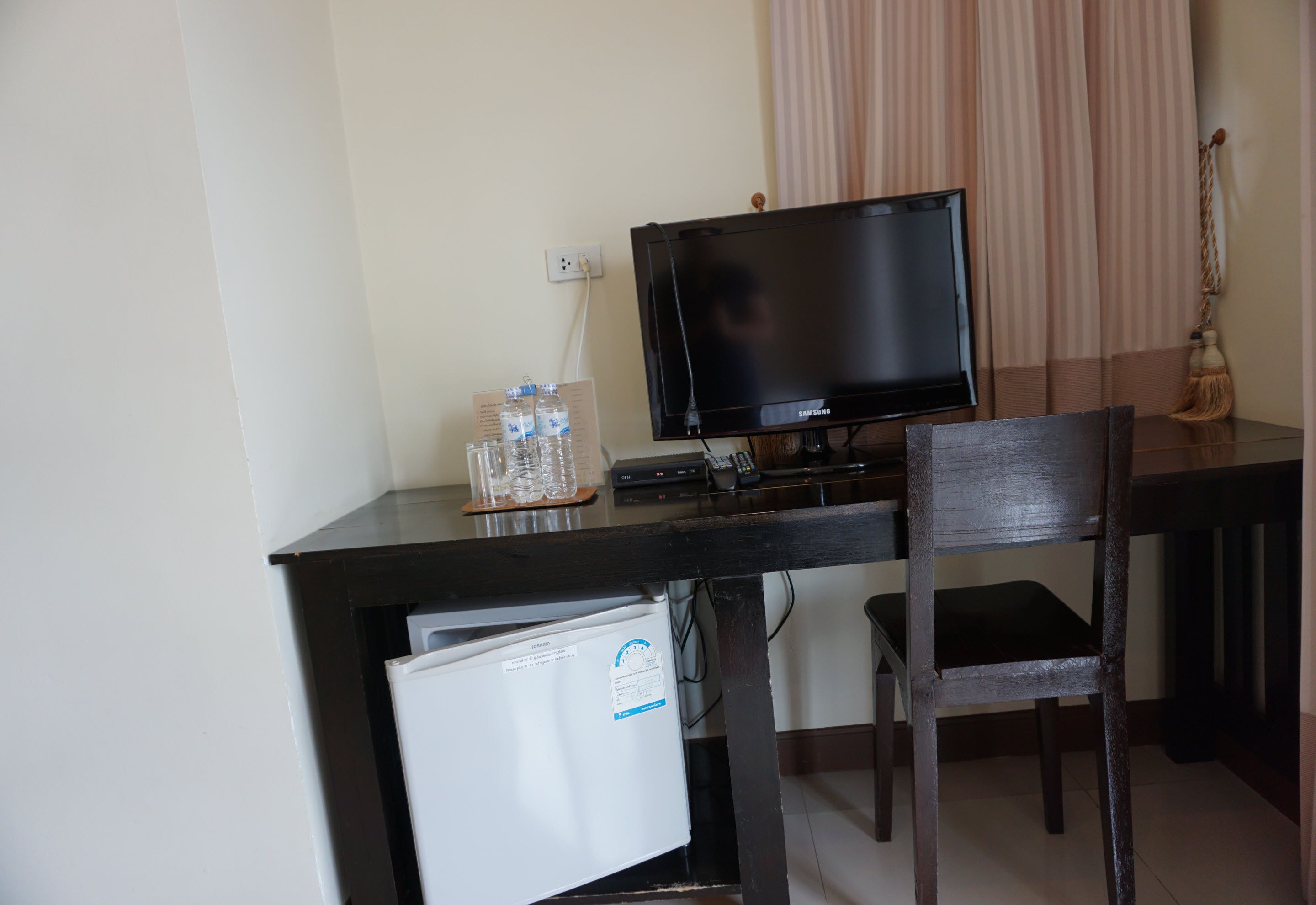 Une chambre d’hôtel équipée d’un bureau, d’une télévision, d’un réfrigérateur et d’une chaise.