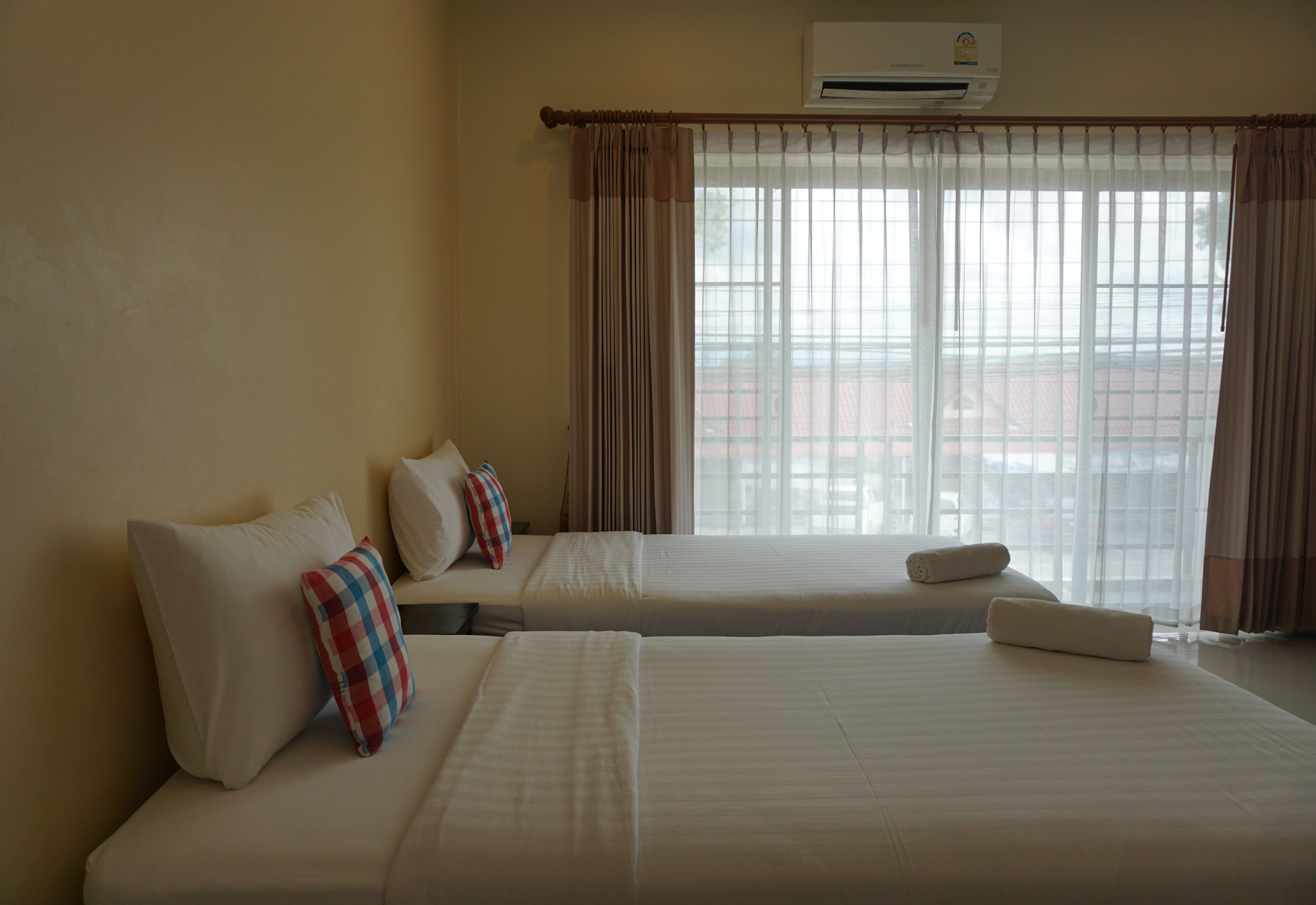 A hotel room with two beds, a window with curtains, and an air conditioning unit.