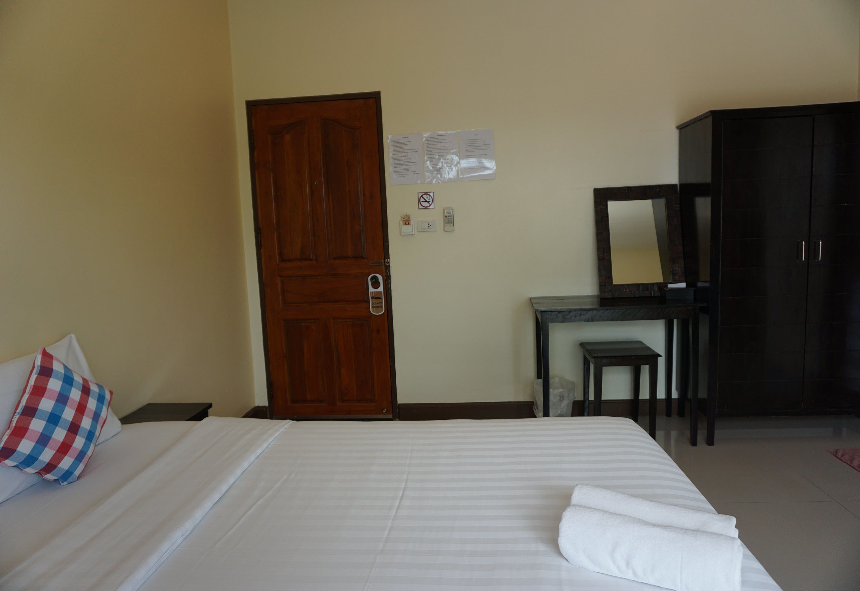 Habitación de hotel con cama, puerta de madera, escritorio con silla, armario y espejo.