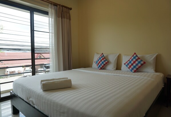 A hotel room with a large bed, two pillows, a window with curtains, and a view of buildings outside.