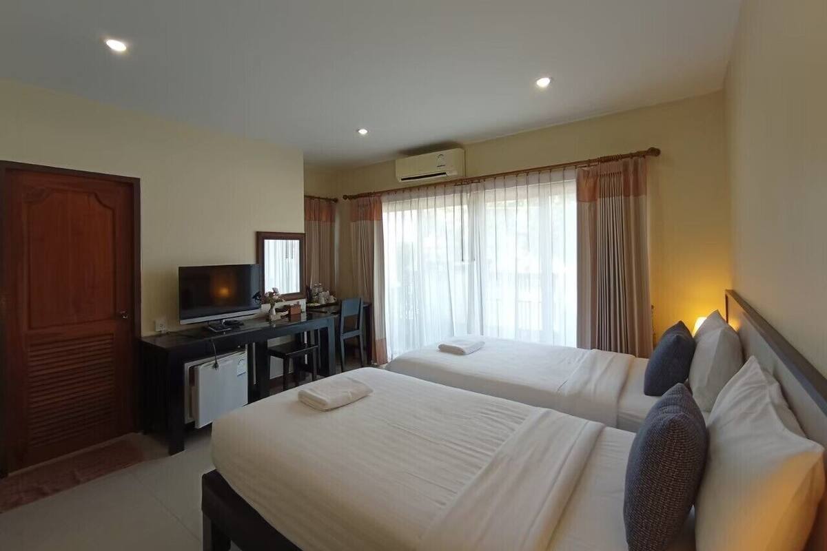 A hotel room with two beds, a desk with a computer, a television, and an air conditioning unit.