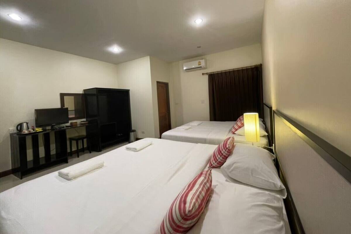 A hotel room with two beds, a TV, a desk with a computer, and an air conditioning unit.