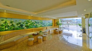 A modern lobby with a large lotus flower mural, comfortable seating, and a glass coffee table. - White Lotus (Lao Cai)