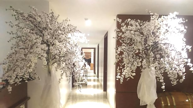 A hallway with white artificial cherry blossom trees, a wooden barrel, and a tiled floor. - White Lotus (Lao Cai)