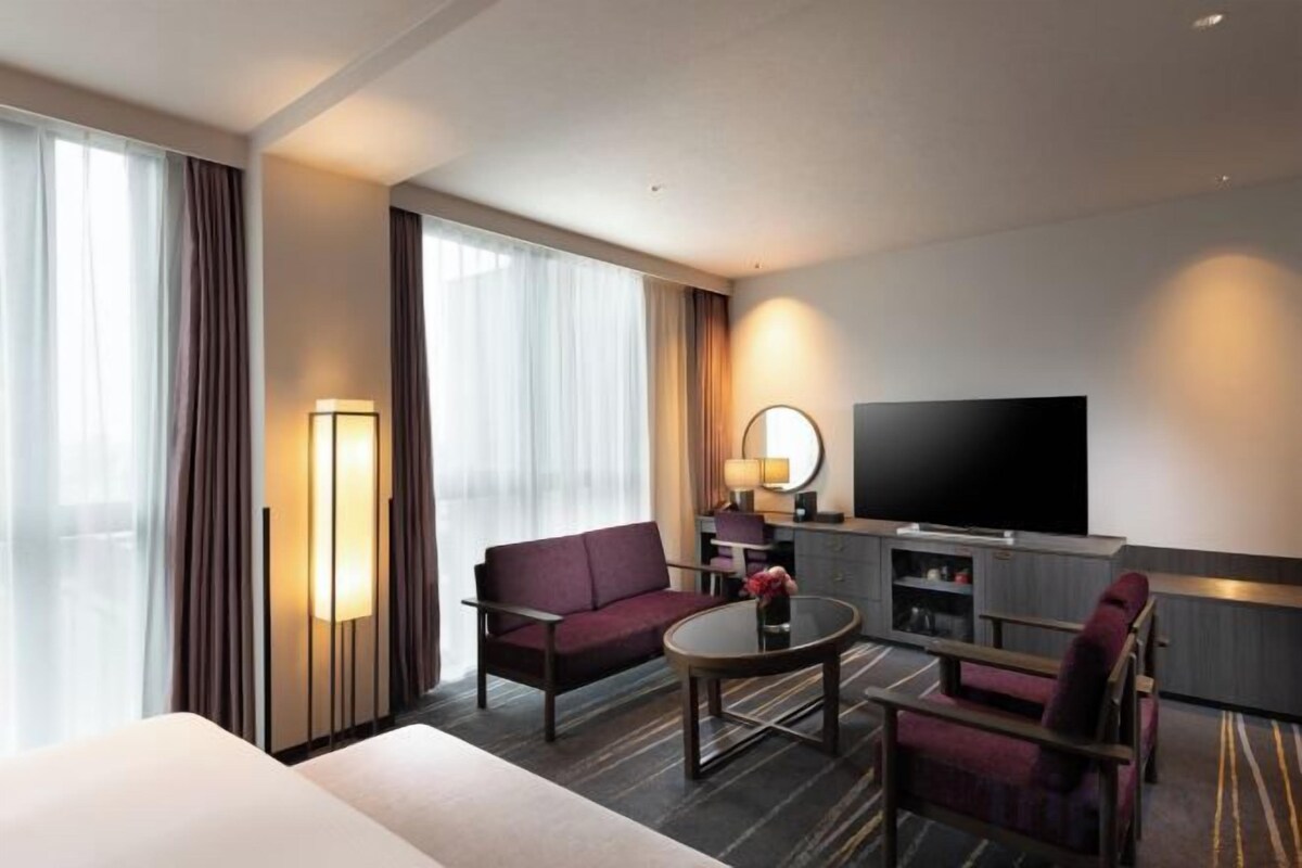 Una habitación de hotel con cama, sofá, una mesita, televisión y lámpara.