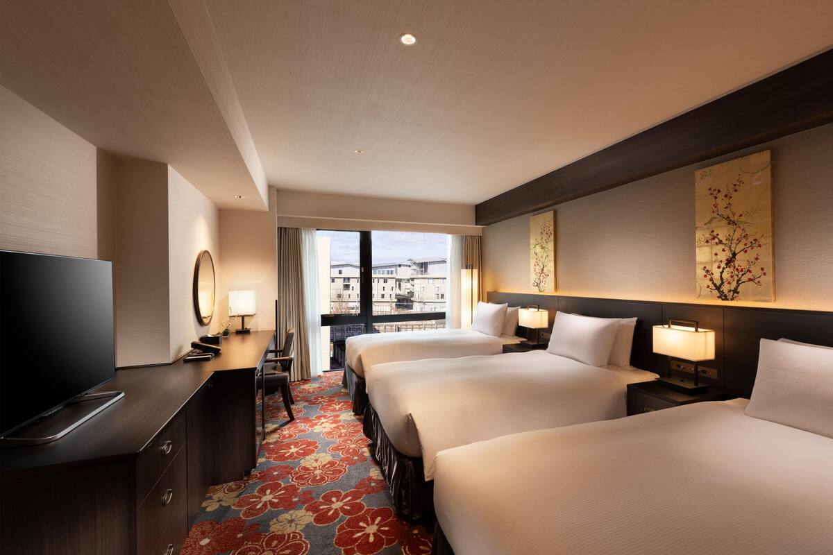 Camera d'albergo con due letti, televisione, scrivania e vista sugli edifici.