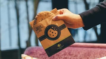 A hand holding a bag with a cookie and a label indicating it contains walnuts, wheat flour, egg, and milk.