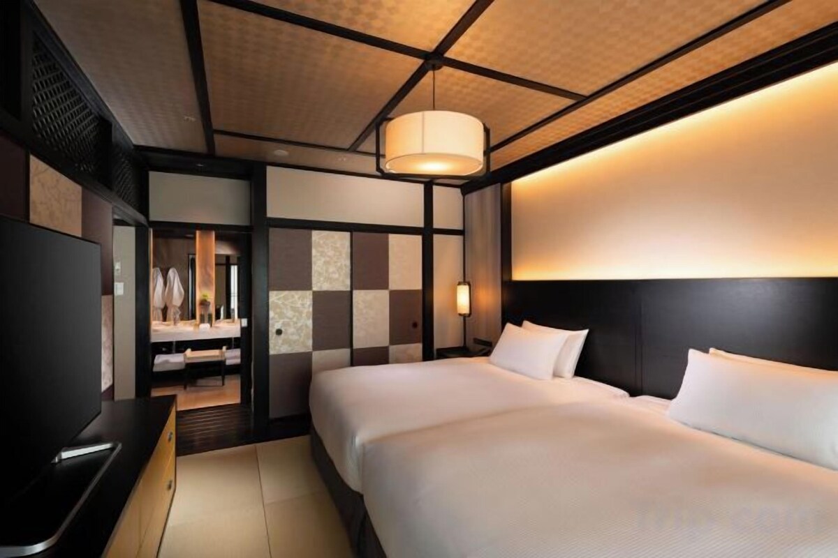 Habitación de hotel con cama, televisión y baño con espejo y toallero.